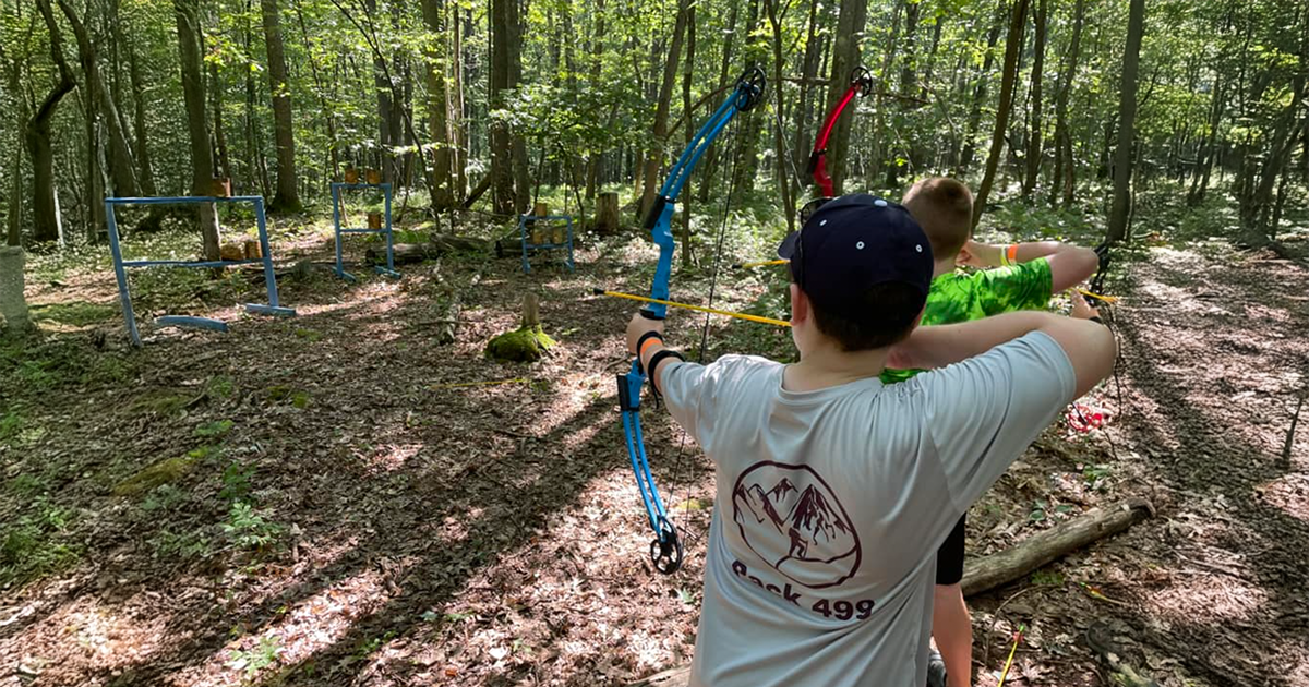 scouts shooting bow and arrow in a shaded wood.